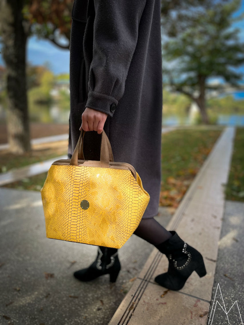 Photo d'une jeune femme blanche et blonde portant un sac à main jaune et marron, dans un parc en extérieur, de jour.