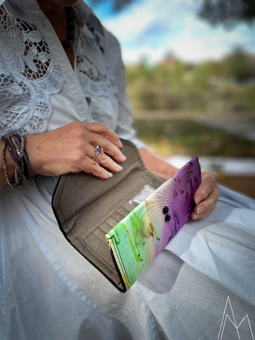Photo d'une femme blanche mûre portant un portefeuille dans les tons verts et violets, dans un parc en extérieur, de jour.