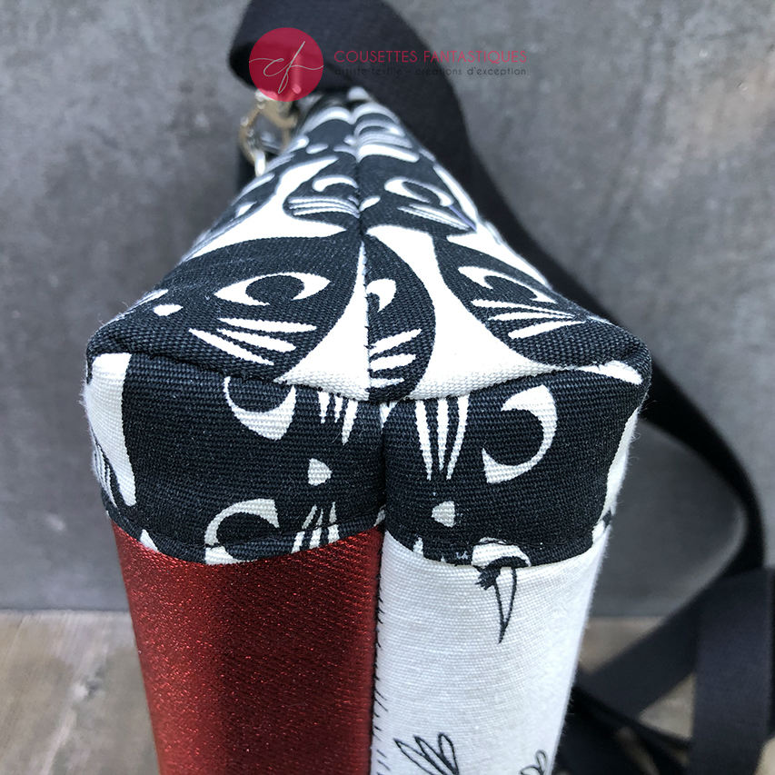 A trapezoid messenger bag made from black and white cotton fabrics on the outside with stylized cat and bird motifs, matched with bird-themed cotton cretonne on the inside.