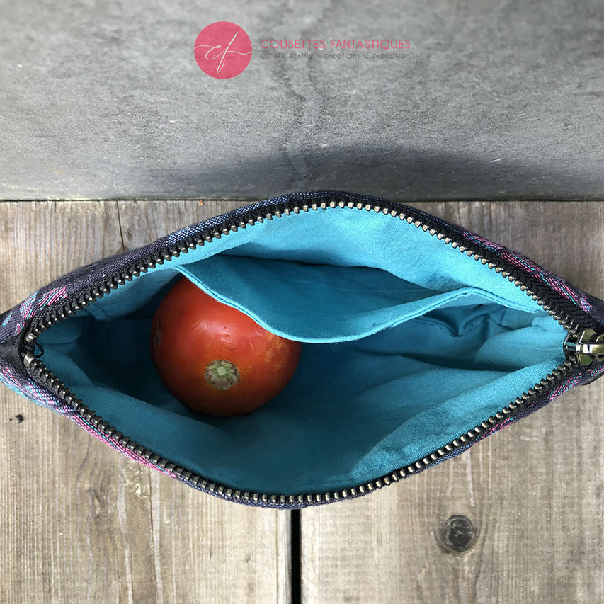A small zippered pouch sewn in gray faux leather and a white and gray babywearing scarf with a feather pattern.