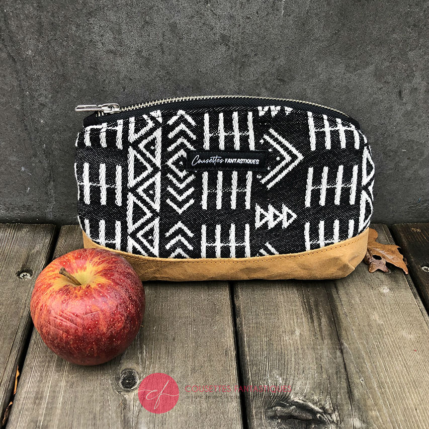 A small zippered clutch made of washable caramel paper, a black and white geometric patterned babywearing wrap, and grey poplin.