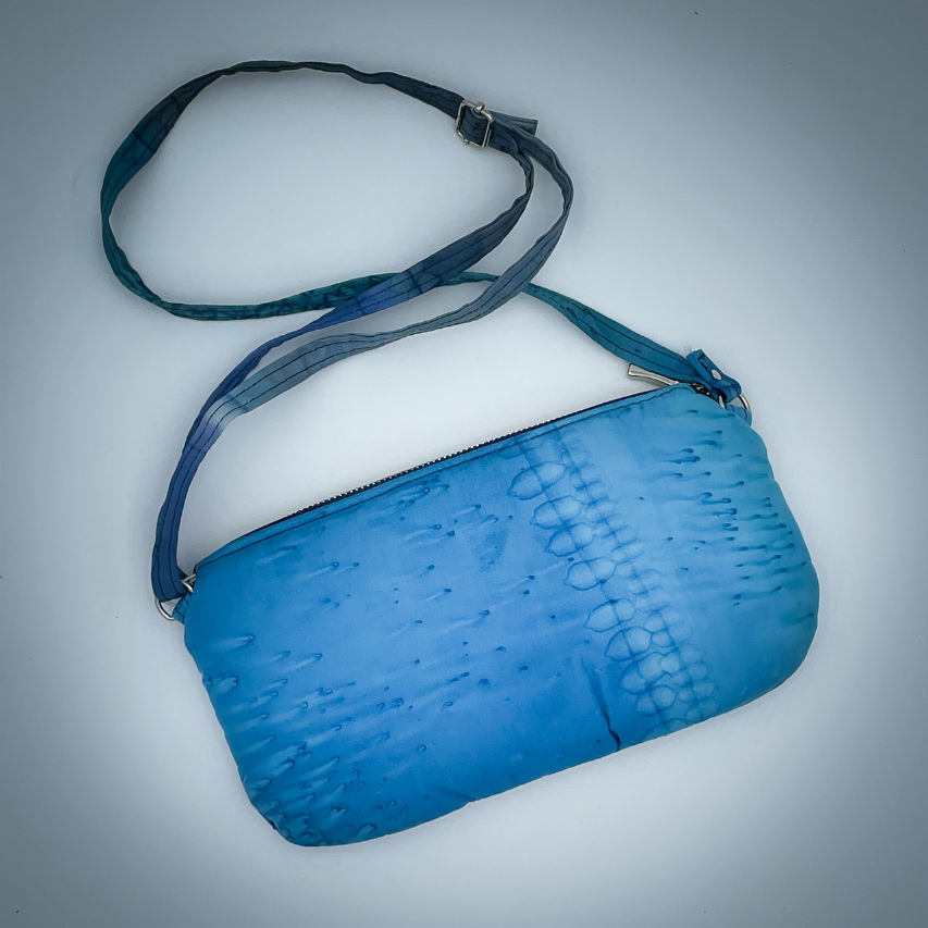 Une pochette zippée cousue dans un foulard en soie dans les tons bleus, plissé et associé à du liège bleur roi.