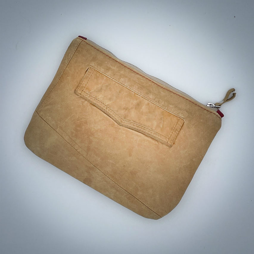 Une pochette zippée cousue dans un cuir de couleur camel et une toile en polycoton avec un motif de feuilles de Ginkgo Biloba rouges.