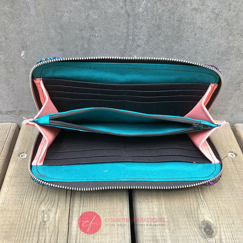 A wallet made with a babywearing wrap in a gradient from blue to violet on the outside and black, pink, and petrol poplin on the inside.