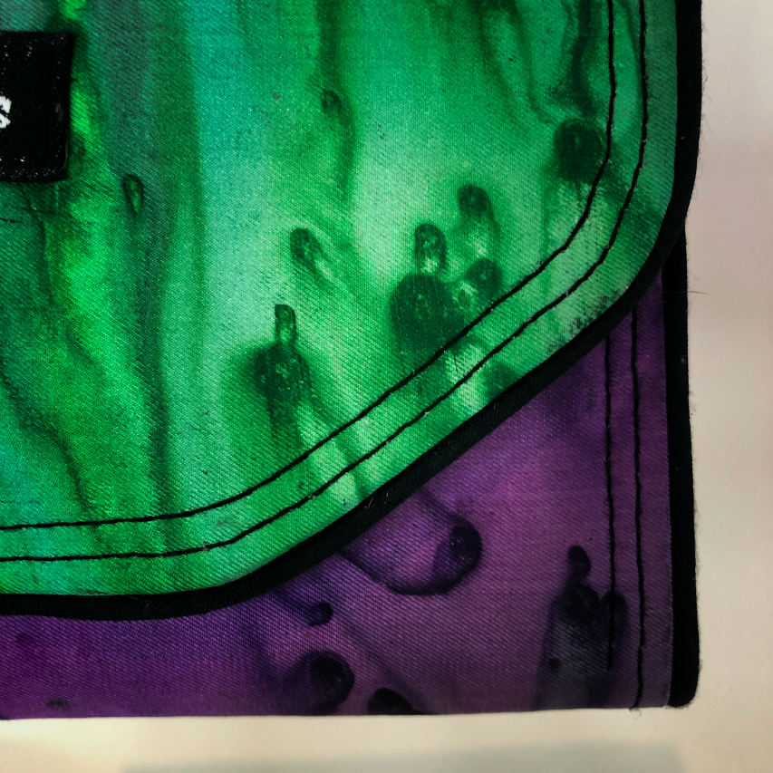 Un portefeuille fait en voile de soie bleu, vert et violet associé à du cuir d'agneau noir à l'extérieur, et en popeline taupe à l'intérieur.