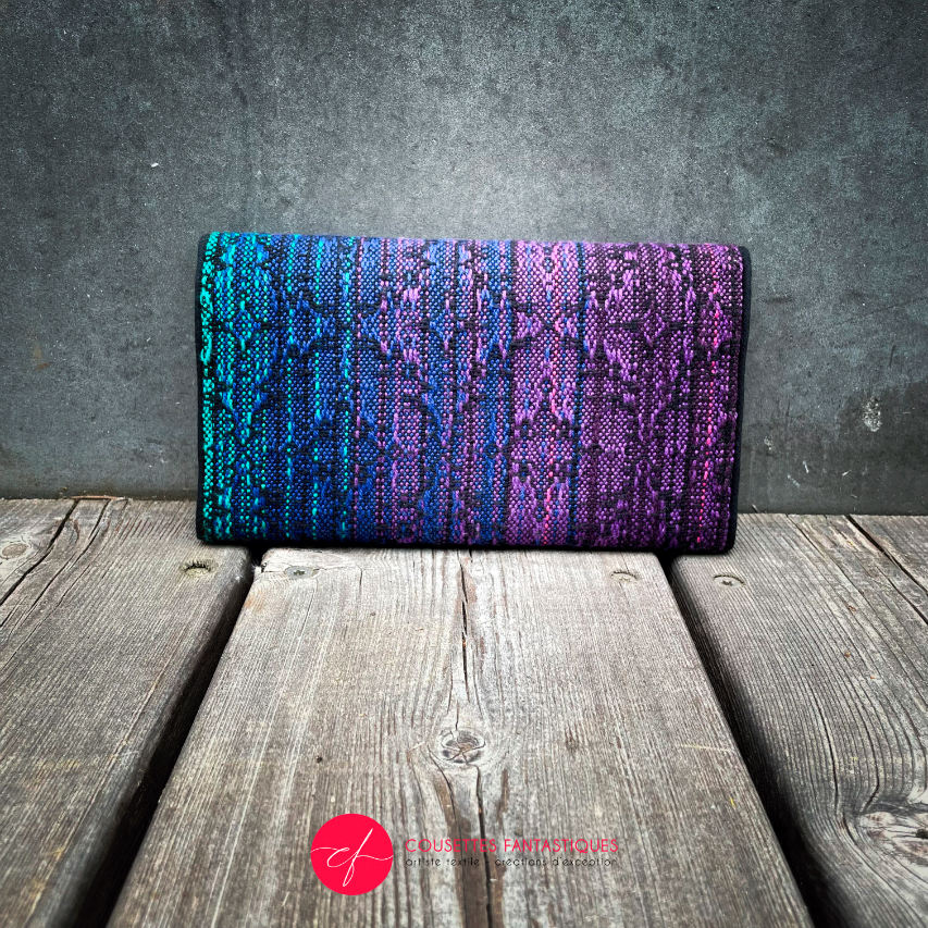 A wallet made from a gradient blue to violet babywearing wrap on the outside and purple voile on the inside.