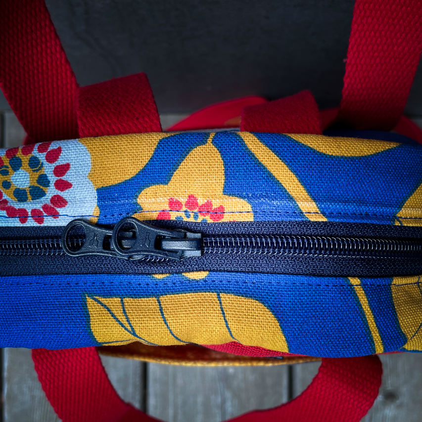 Un sac à dos fait en toile bleue roi à motifs floraux jaunes, blancs et rouges et toile rouge gaufrée à l'extérieur, popelines unies rouges et jaunes à l'intérieur.