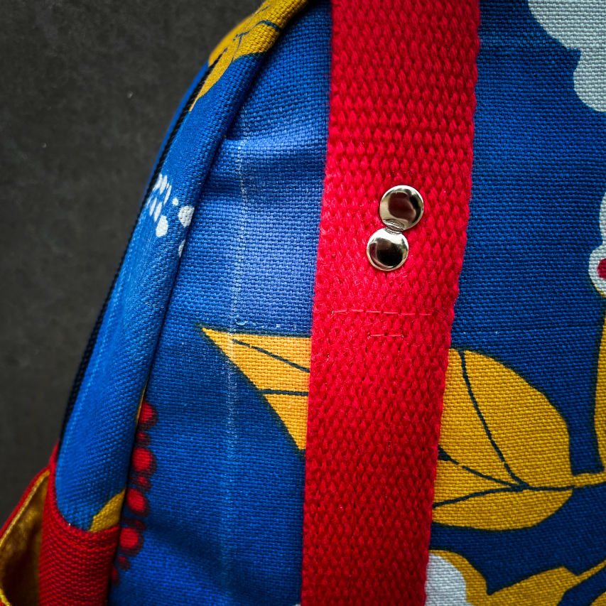 Un sac à dos fait en toile bleue roi à motifs floraux jaunes, blancs et rouges et toile rouge gaufrée à l'extérieur, popelines unies rouges et jaunes à l'intérieur.