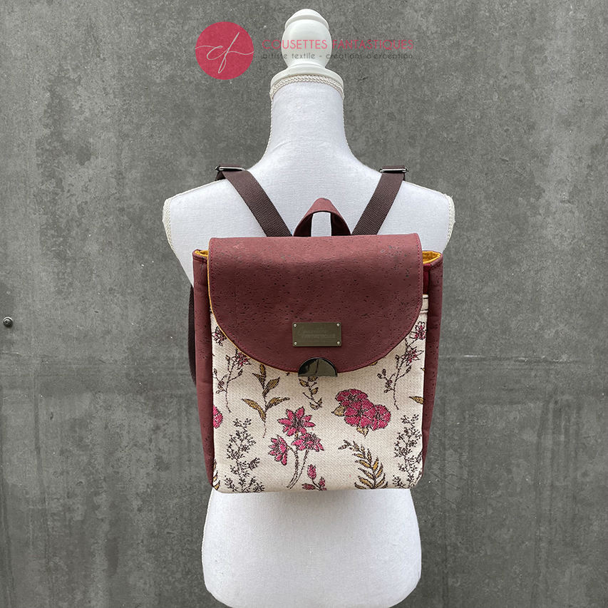 A backpack made with scarf fabric in floral patterns in pink tones on ecru background and brick cork.