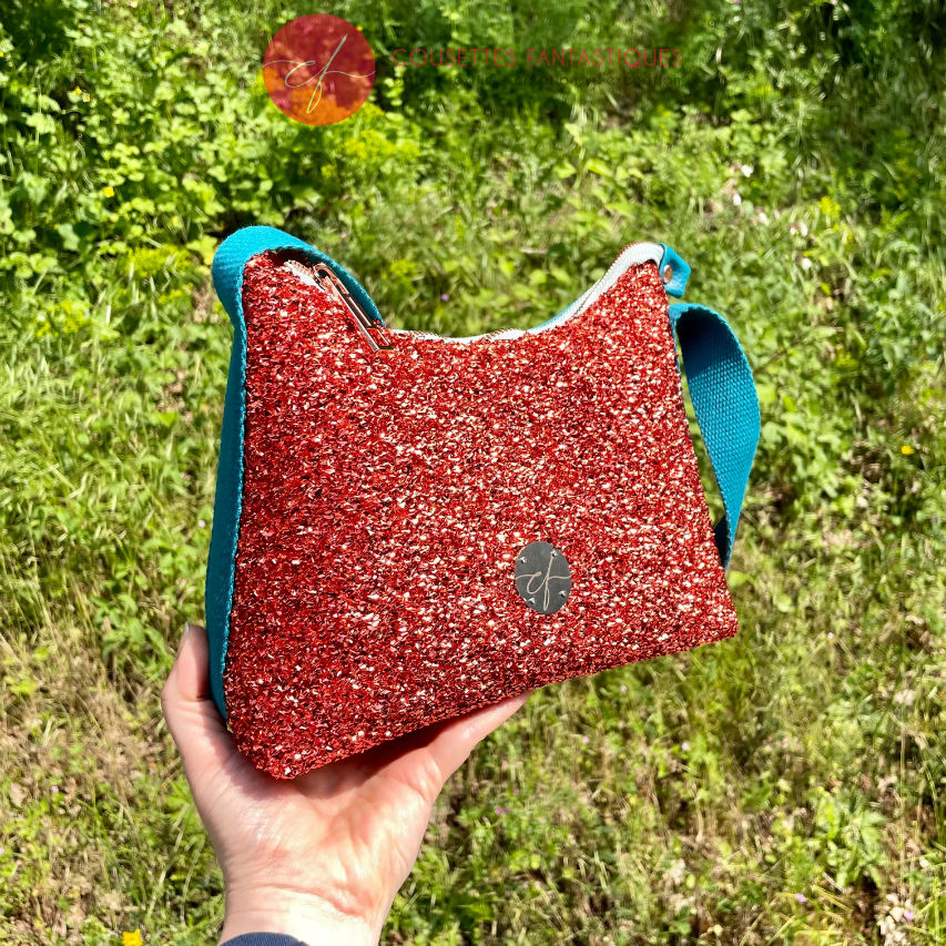 Un petit sac bandoulière zippé fabriqué à partir d'un tissu extensible avec du bouclé métallique cuivré, du simili bleu turquoise, et une doublure orange clair lumineuse.