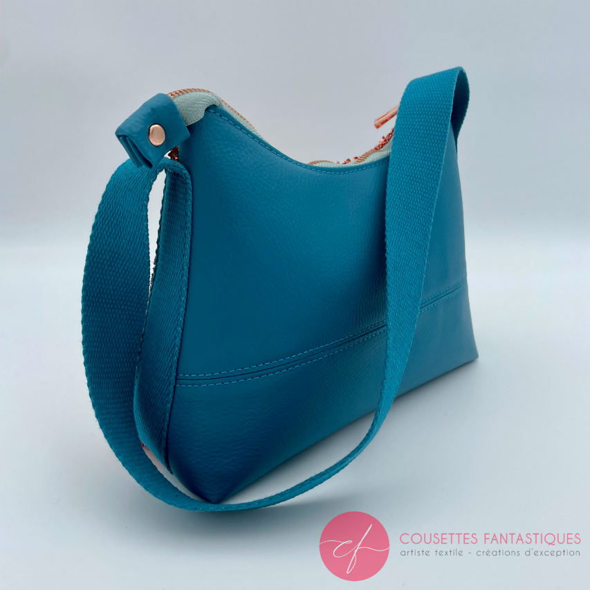 Un petit sac bandoulière zippé fabriqué à partir d'un tissu extensible avec du bouclé métallique cuivré, du simili bleu turquoise, et une doublure orange clair lumineuse.