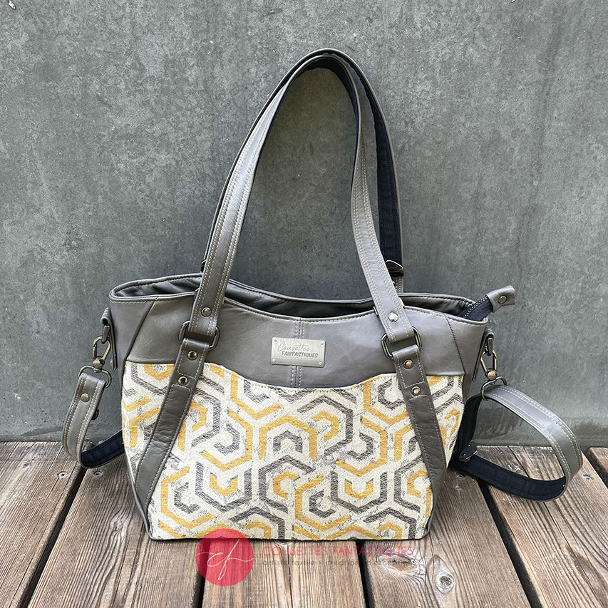 A shoulder bag made from gray, mustard, and ecru babywearing wrap with geometric patterns, and gray lamb leather.