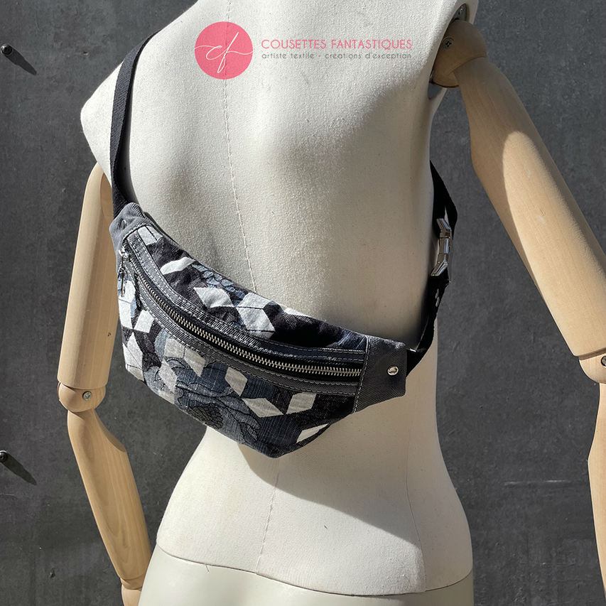 A fanny pack made from babywearing fabric in gray, white, and blue tones with a floral and geometric pattern and gray denim.