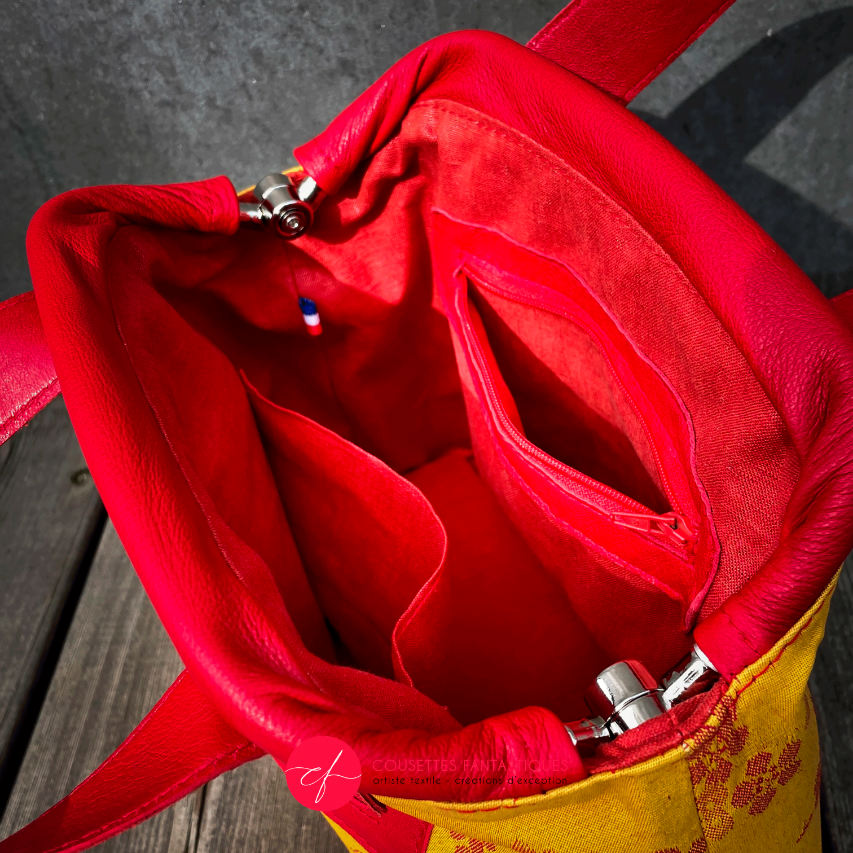 Un mini sac à main constitué de tissu d'ameublement jaune motif fleurs de cerisier rouge et de cuir rouge.