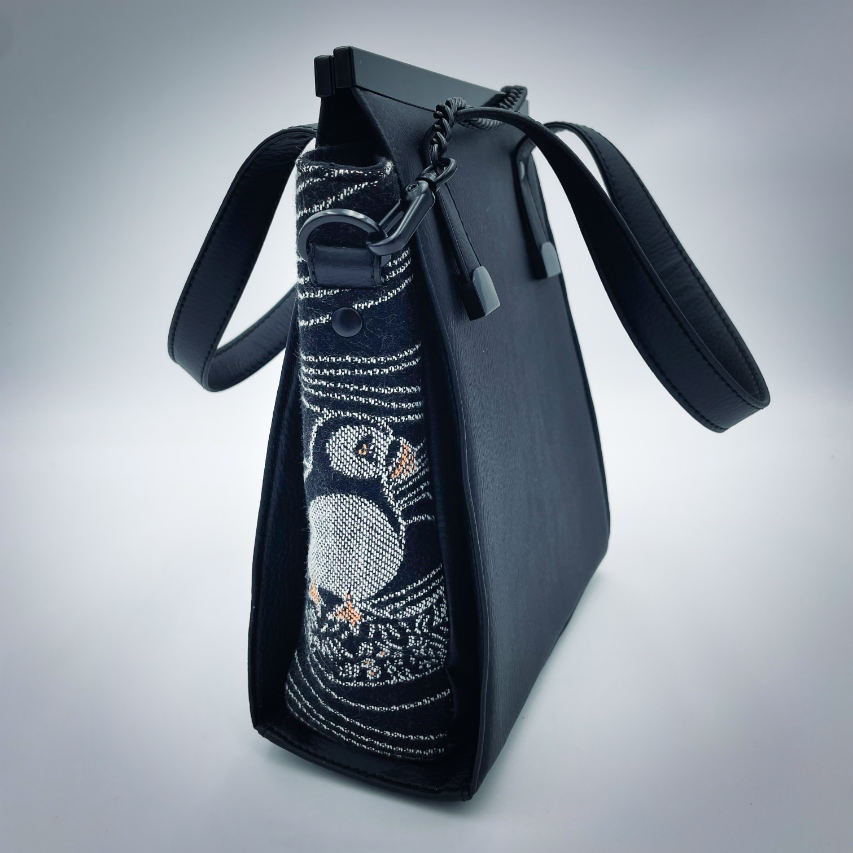 Un petit sac à main confectionné à partir d'écharpe de portage au motif de macareux dans des vagues stylisées dans des tons noirs, blancs et orange, et du simili noir.
