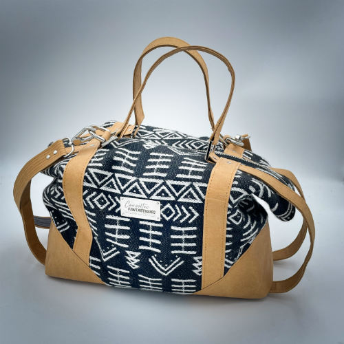 Un petit sac de voyage fabriqué en papier lavable couleur caramel, une écharpe de portage à motif géométrique noir et blanc, et de la popeline grise.