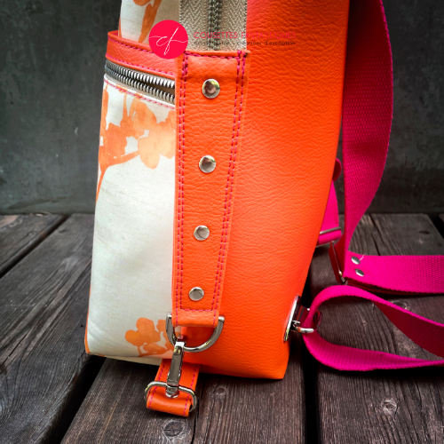 Un sac à dos confectionné en simili orange vif et en tissu d'ameublement crème au motif végétal dégradé de rose à orange.