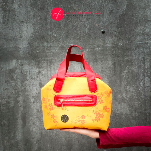 Un mini sac à main constitué de tissu d'ameublement jaune motif fleurs de cerisier rouge et de cuir rouge.