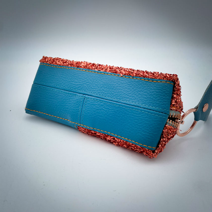 Une pochette zippée fabriquée à partir d'un tissu extensible avec du bouclé métallique cuivré, du similicuir bleu turquoise, et une doublure menthe clair.